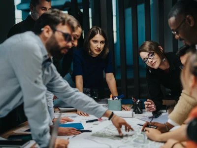 Gruppe von Menschen beugt sich über einen Arbeitstisch voller Papiere